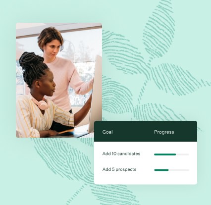 Two women pointing at a desktop monitor collaborating next to goals progress UI screen 213x207